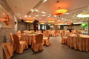 A banquet hall with round tables, chairs, and overhead lighting fixtures. - Songling Hotel (Suzhou)