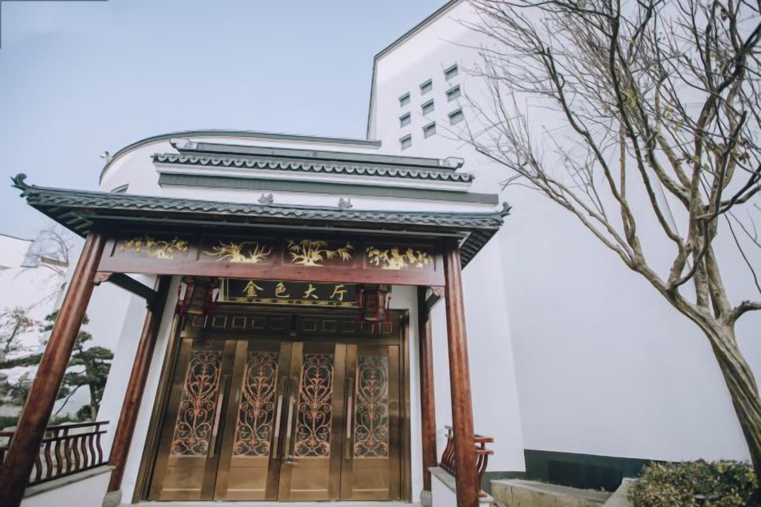 A traditional Chinese gate with intricate woodwork and a modern building in the background.