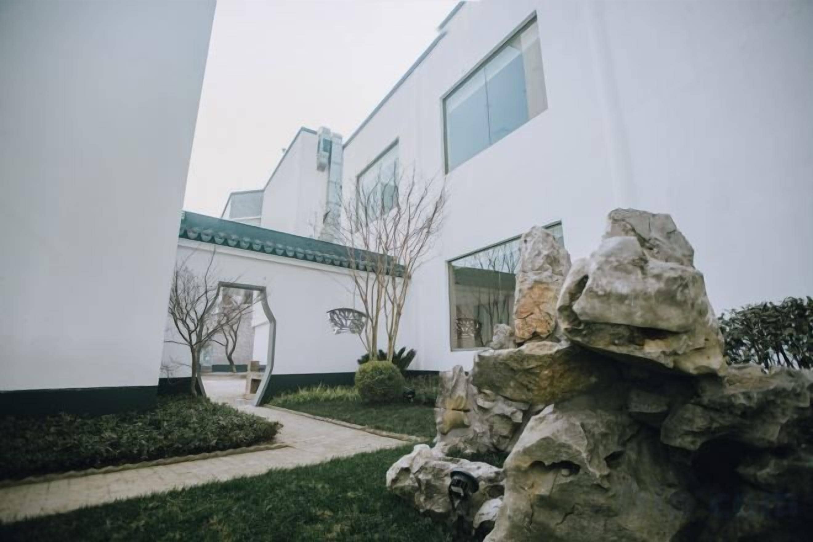 Un edificio moderno con fachada blanca, un sendero de piedra y una formación rocosa al frente.
