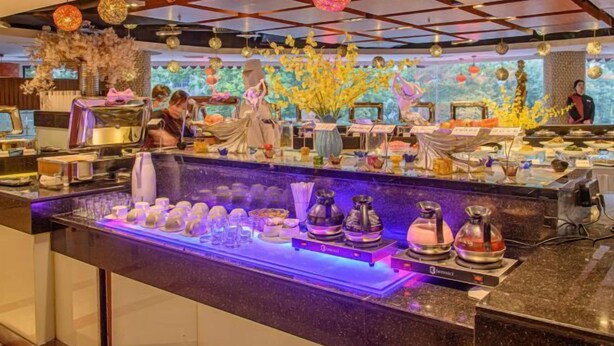 A buffet area with a variety of dishes and beverages, a person serving, and decorative elements like hanging lanterns and floral arrangements. - Songling Hotel (Suzhou)