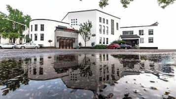 A white building with a reflection in a puddle, a red car, and a tree.