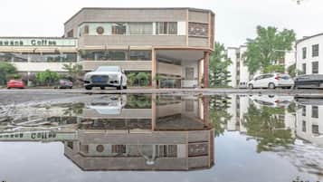A building with a reflection in a puddle, a car in front, and a coffee shop in the background.
