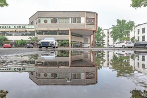 A building with a reflection in a puddle, a car in front, and a coffee shop in the background. - Songling Hotel (Suzhou)