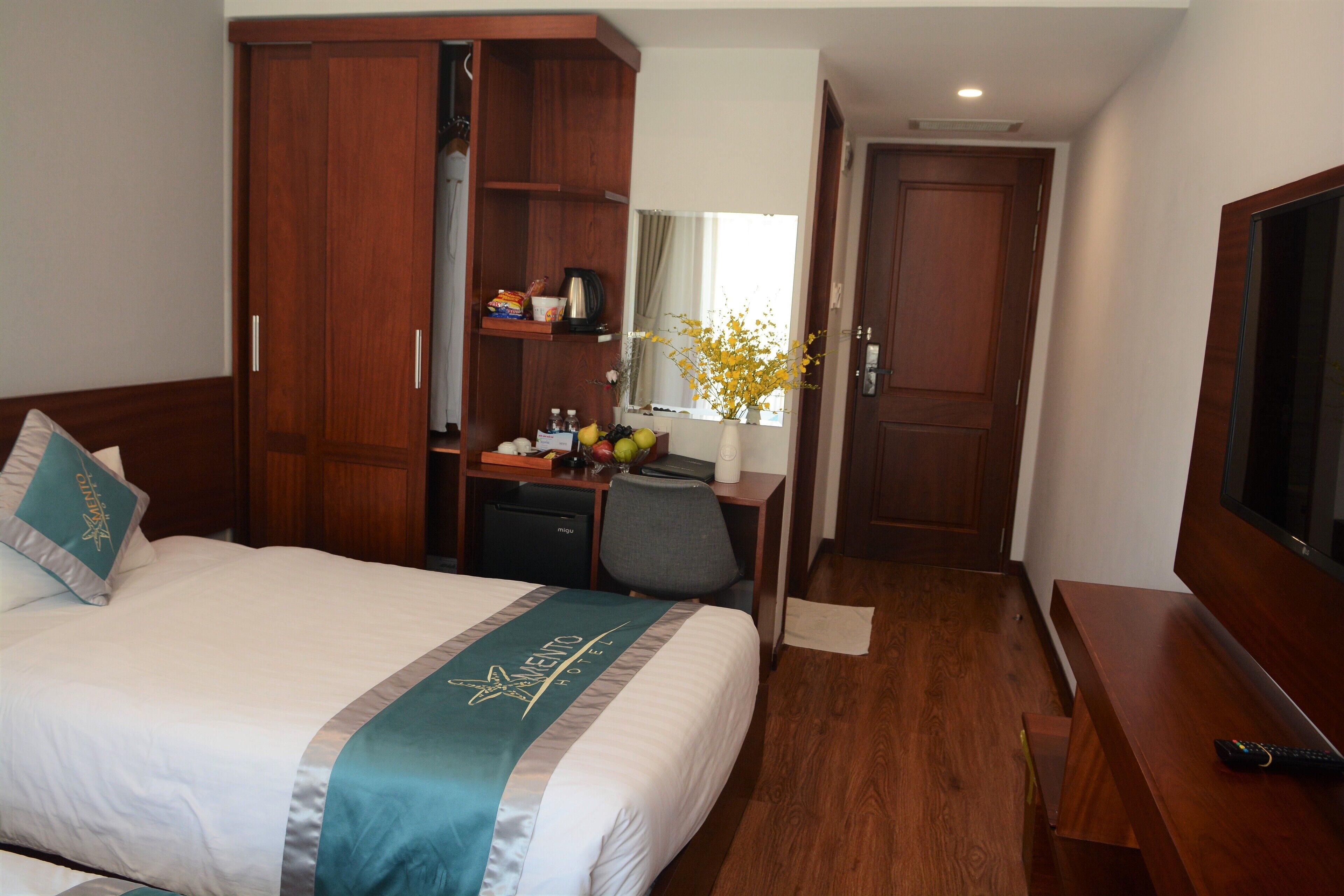 A hotel room with a bed, a desk with a computer, a TV, and a wardrobe.