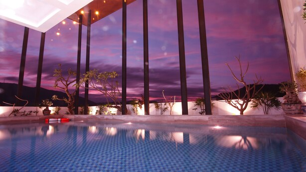 Une piscine offrant une vue imprenable sur le coucher du soleil, entourée de grands palmiers et dotée d’une architecture moderne.