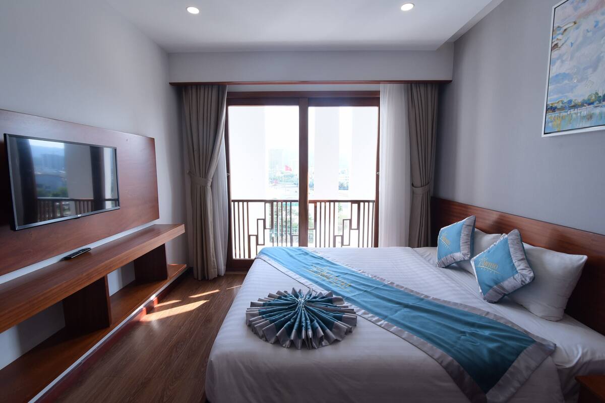 Ein Hotelzimmer mit einem großen Bett, einem Fernseher auf einem Holzbalken und einem Balkon mit Vorhängen.