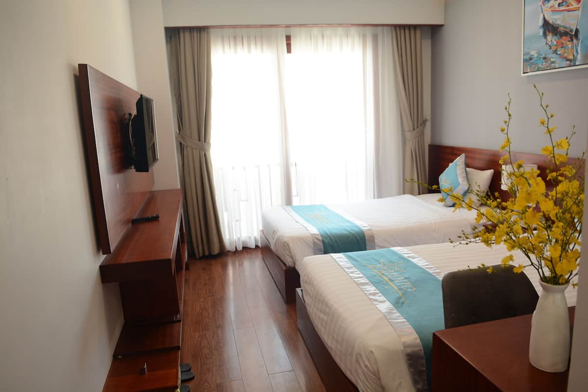 Ein Hotelzimmer mit zwei Betten, einem Holztisch, einem Stuhl, einer Vase mit Blumen und einem Bild an der Wand.