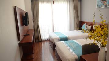 Habitación de hotel con dos camas, un escritorio de madera, una silla, un jarrón con flores y un cuadro en la pared.