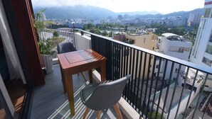 Un balcon avec une table et des chaises, donnant sur un paysage urbain avec des bâtiments et des montagnes.