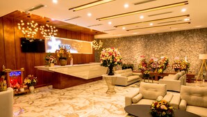 Un espace d’accueil d’hôtel au design moderne, comprenant un comptoir d’accueil en bois, un mur en pierre et plusieurs coins salon agrémentés de compositions florales.