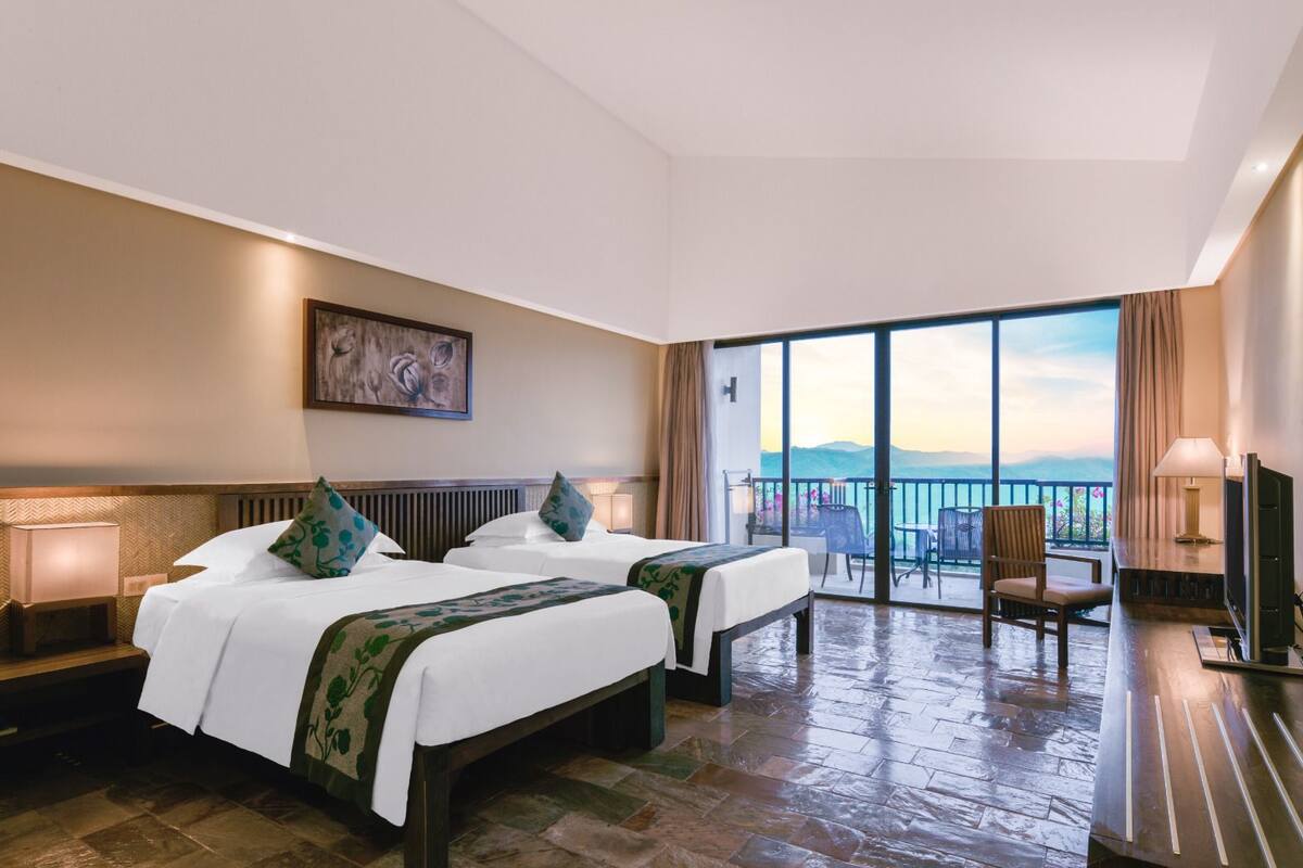 A hotel room with two beds, a TV, a balcony with a view, and a painting on the wall.