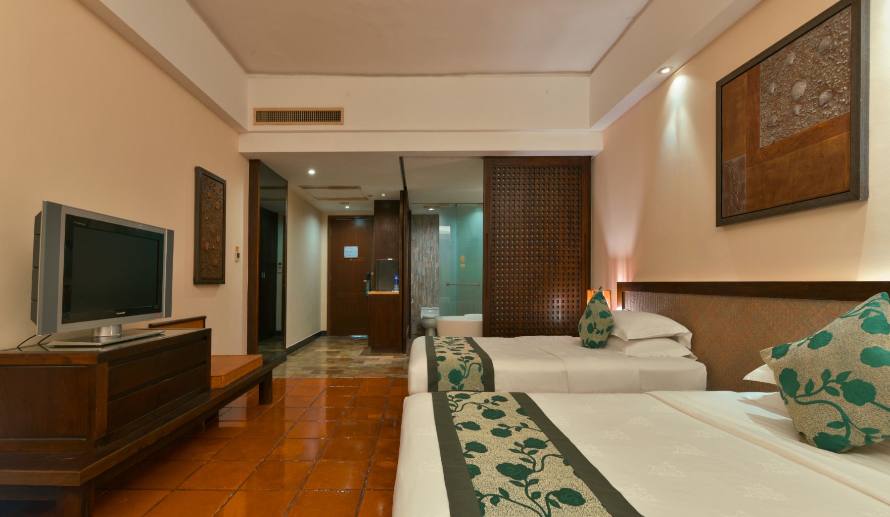 A hotel room with a bed, a TV, a desk, and a bathroom visible through an open door.