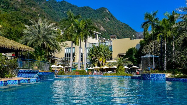 A swimming pool with blue tiles, surrounded by palm trees and a mountain in the background. - Pattra Resort Hotel (Guangzhou)