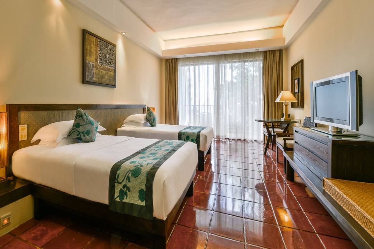 A hotel room with two beds, a television, a desk, and a lamp.