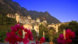 A hotel with multiple buildings, a mountainous backdrop, and a clear sky. - Pattra Resort Hotel (Guangzhou)