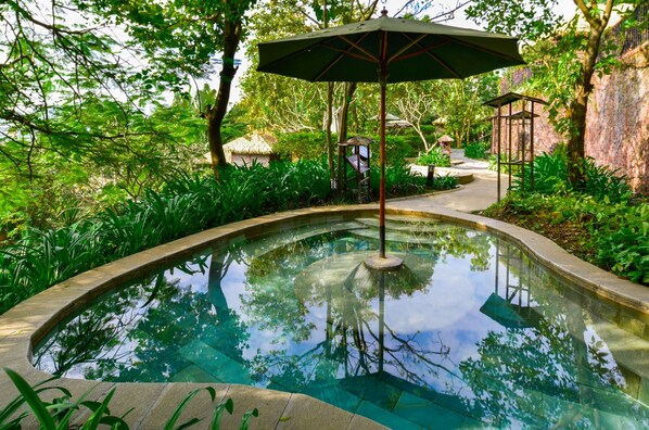 A serene garden with a clear pool, surrounded by lush greenery and a gazebo.