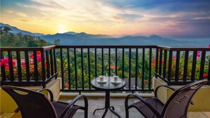 A balcony with a table and chairs, overlooking a mountainous landscape with a sunset. - Pattra Resort Hotel (Guangzhou)