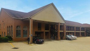 A multi-story building with a brick facade, a covered entrance, and a parking area with cars. - Magnuson Hotel Marietta (Marietta)