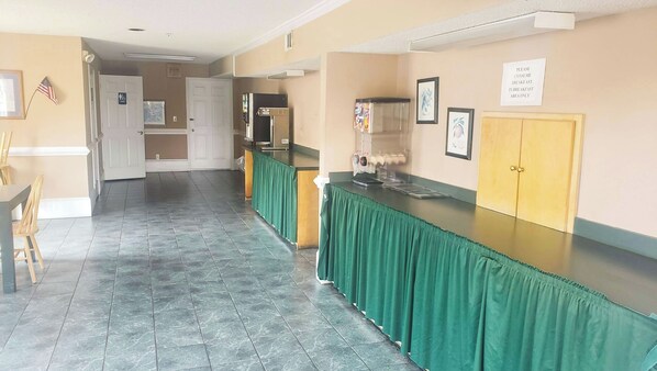 A hotel lobby with a long reception desk, a trash can, and a sign indicating a breakfast area. - Magnuson Hotel Marietta (Marietta)