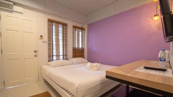 A hotel room with a bed, a desk, a television, and a window with blinds.