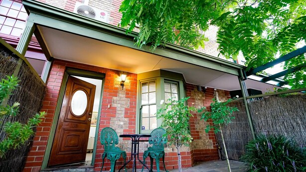 A brick building with a green awning, a wooden door, and two green metal chairs at a small table. - Adelaide Style Accommodation near City (North Adelaide)