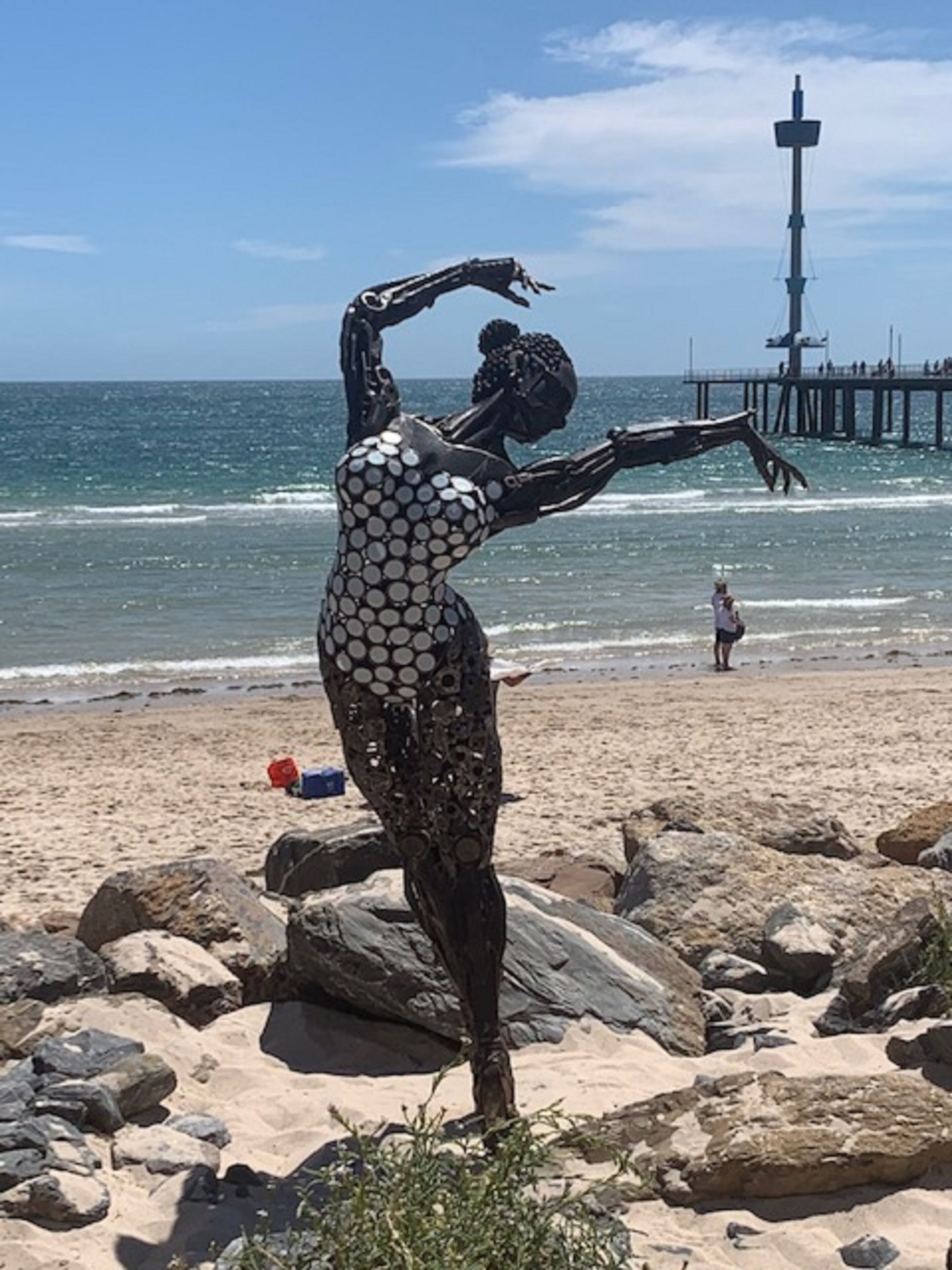 A sculpture on a rocky beach with a pier in the background.
