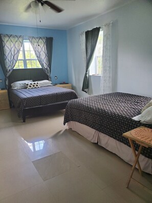 A bedroom with two beds, a ceiling fan, and a window with curtains.