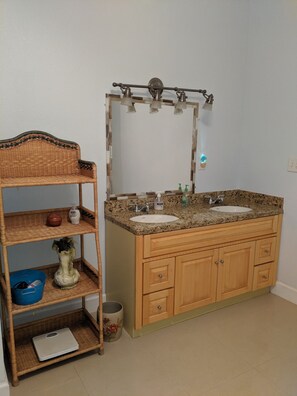 A bathroom with a wooden vanity, a sink, and a mirror. There is a wicker shelf with various items on it.