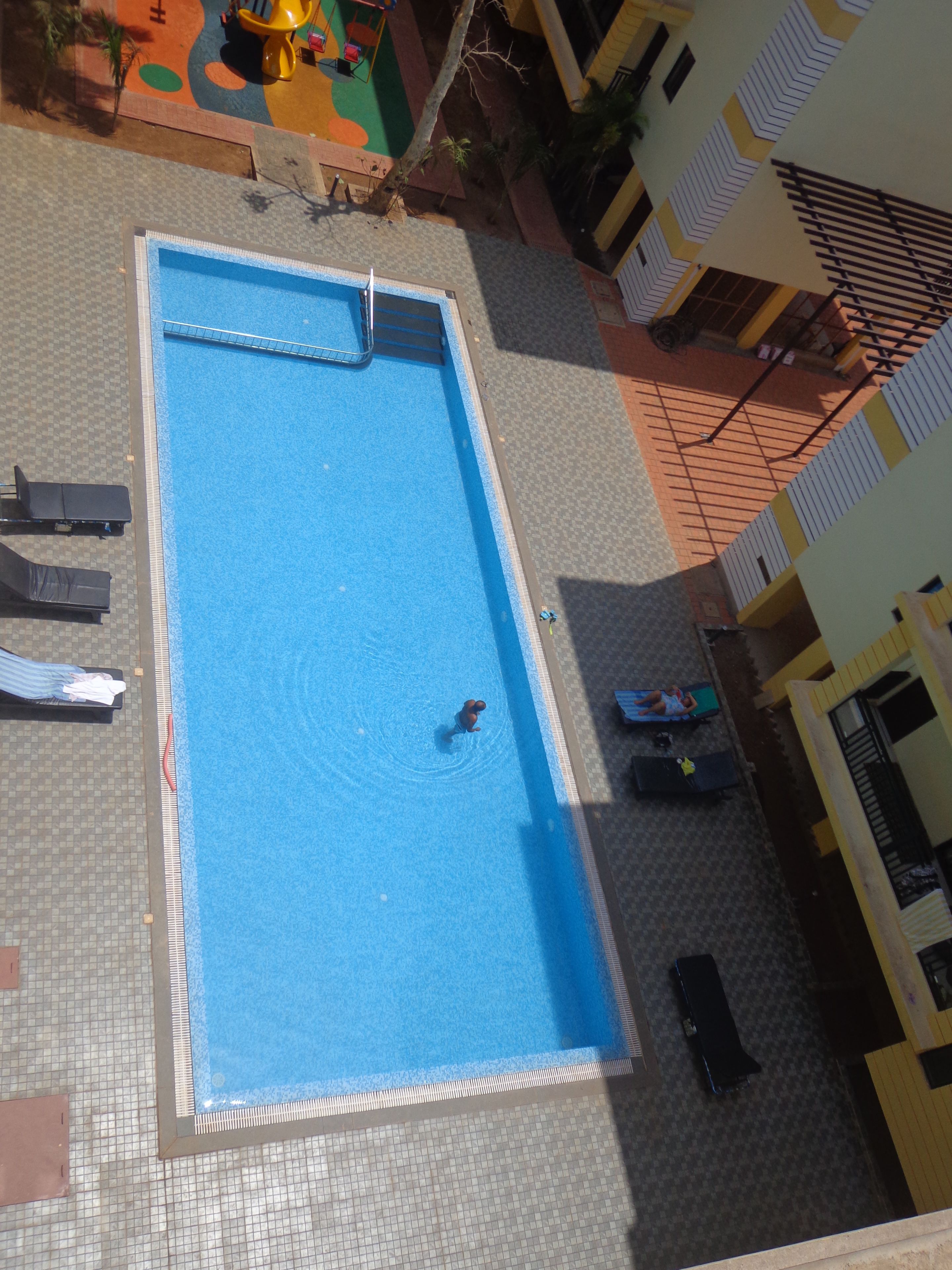 An aerial view of a rectangular swimming pool with a tiled deck surrounding it.