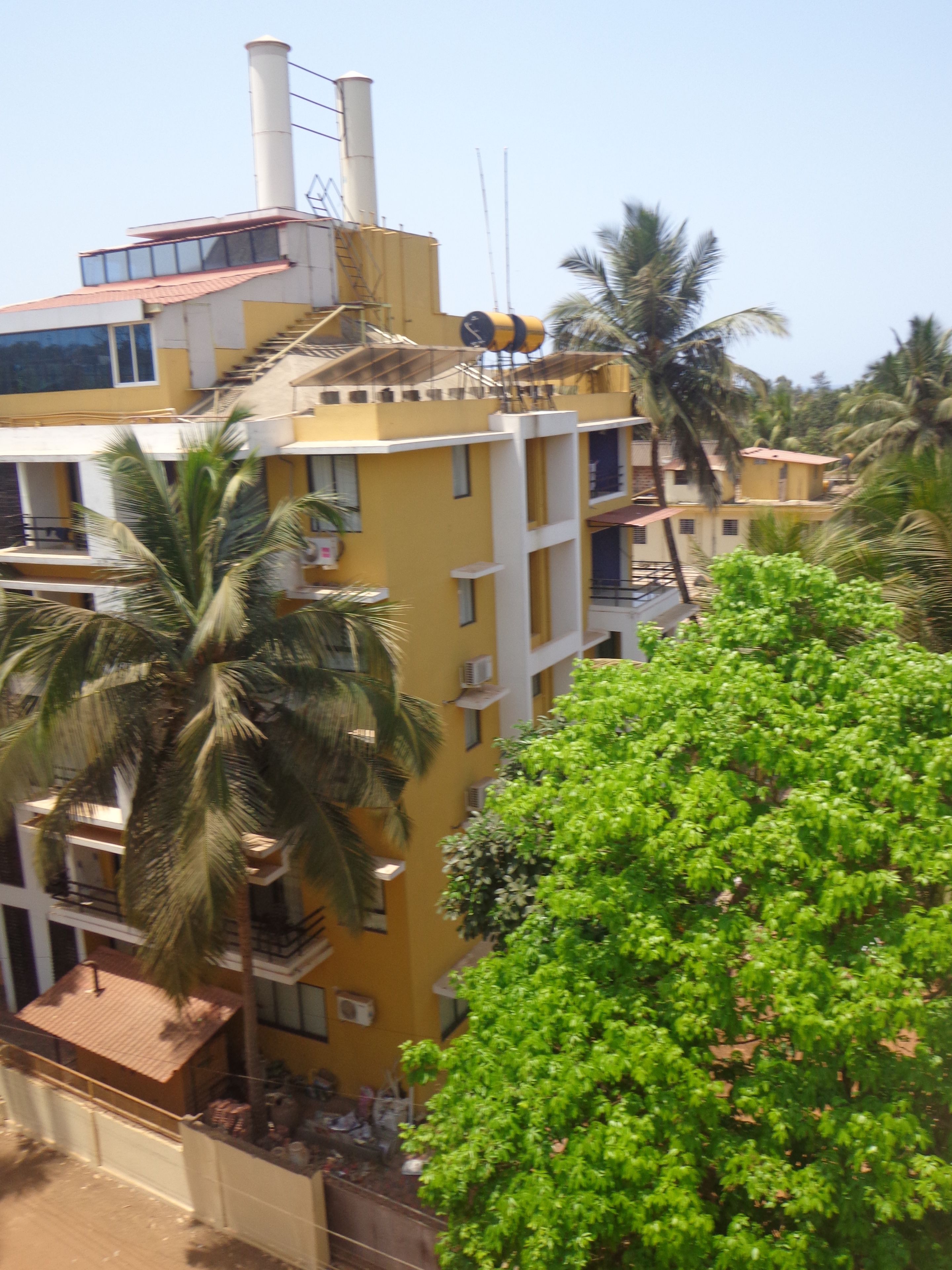 Un edificio amarillo de varios pisos con balcones, rodeado de follaje y palmeras.
