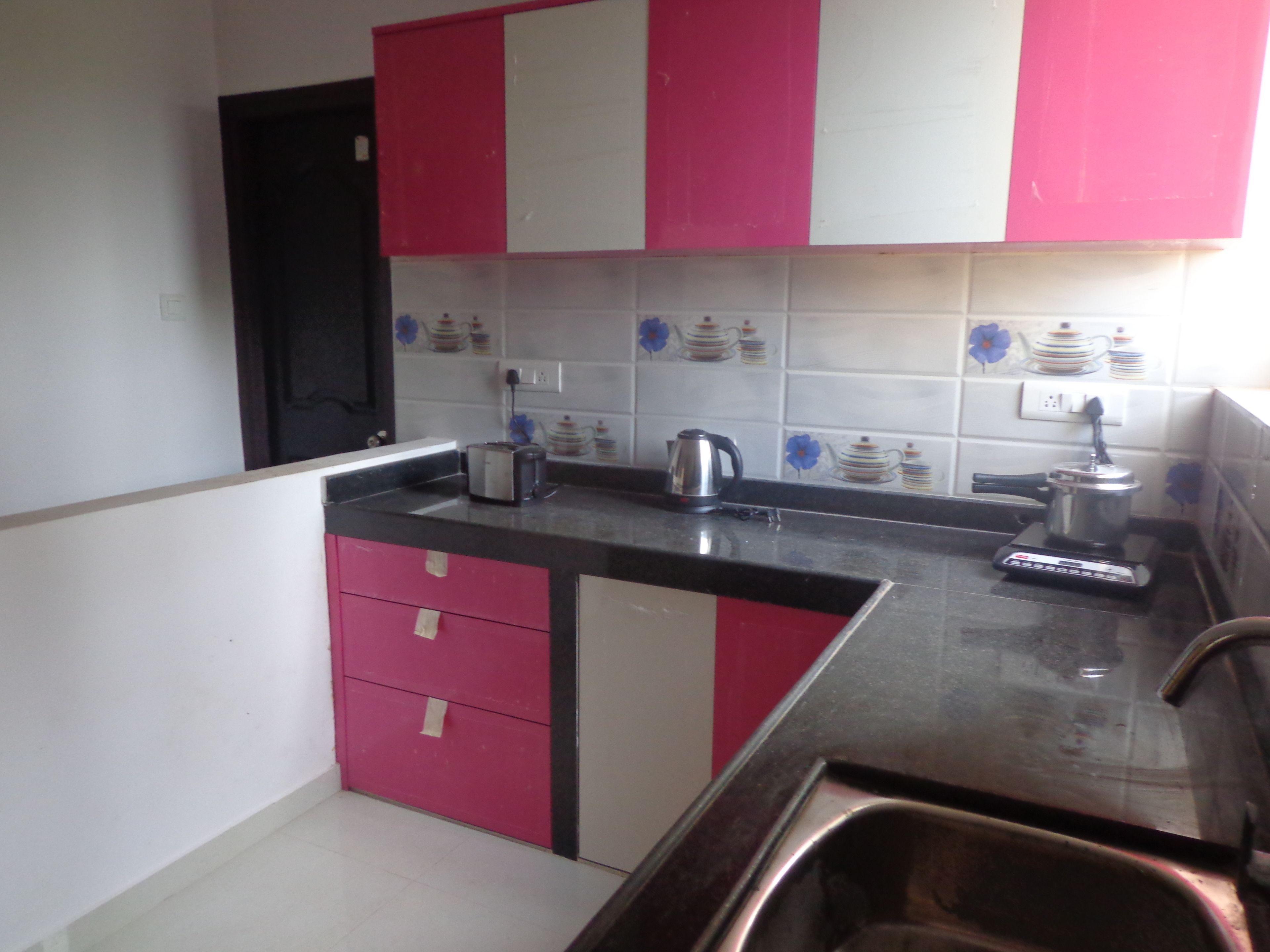 Una cocina con armarios rosa y blancos, un lavamanos de acero inoxidable y una tostadora sobre la encimera.
