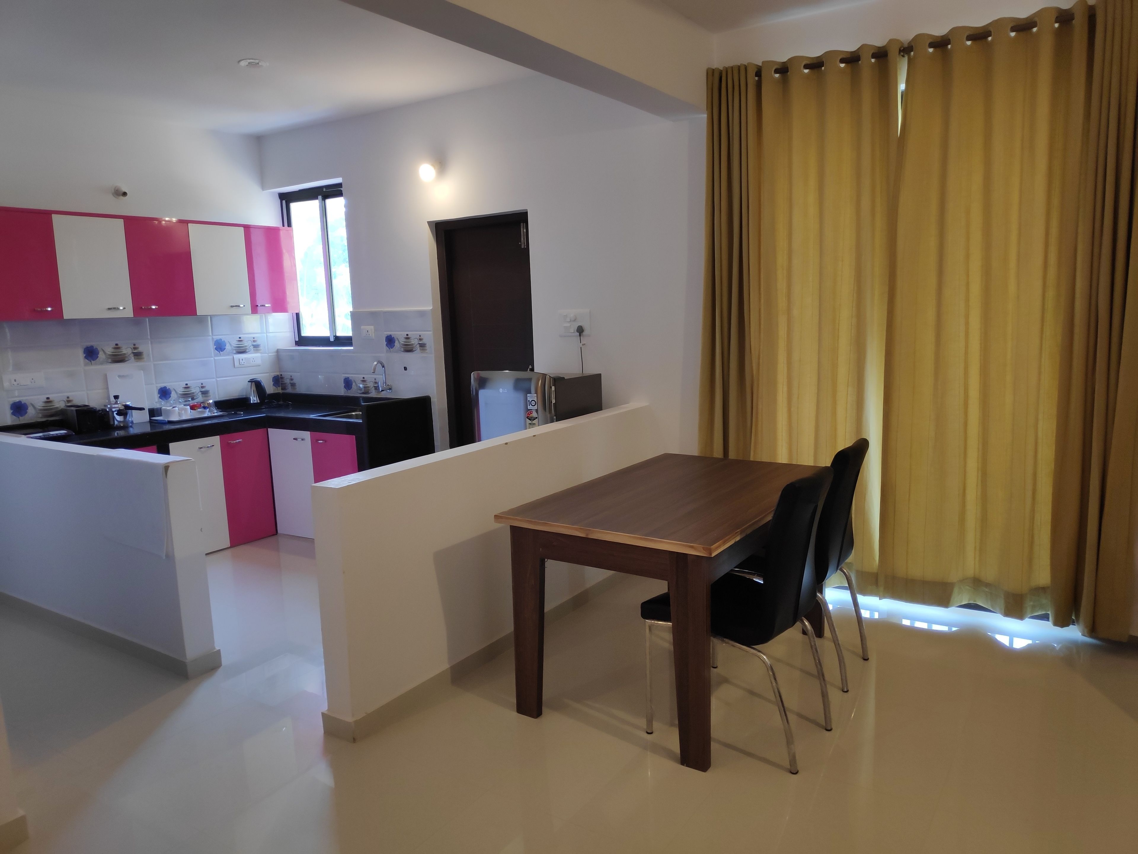 A modern kitchen with pink and white cabinets, a dining table with chairs, and a yellow curtain.