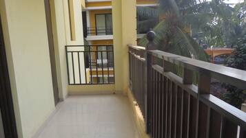 A clean, tiled balcony with a metal railing, a view of a building with balconies, and a palm tree in the background.