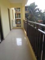 A clean, tiled balcony with a metal railing, a view of a building with balconies, and a palm tree in the background.