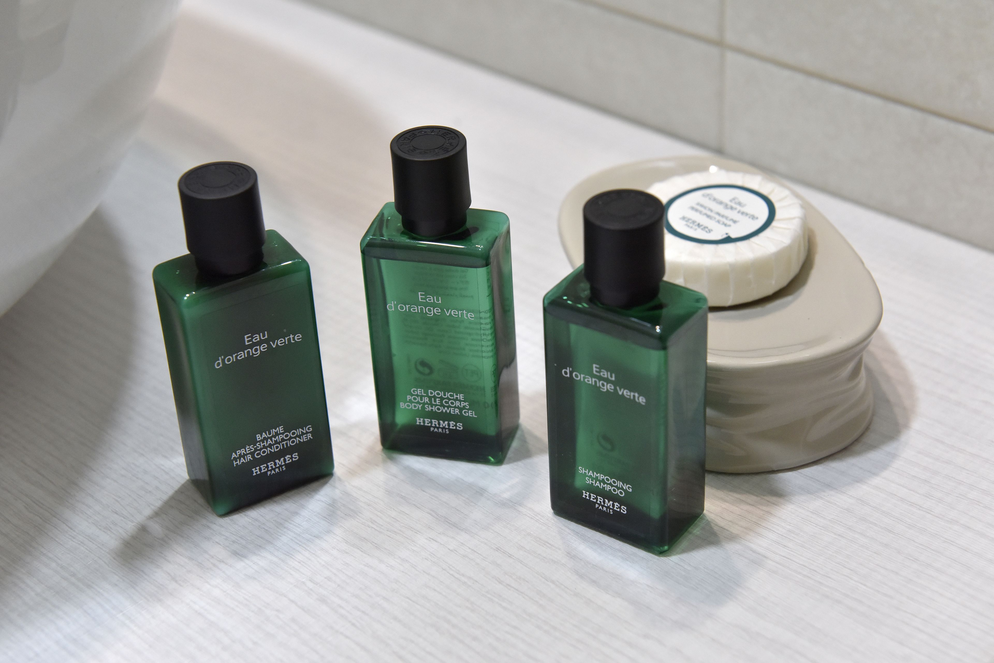 Tre grønne flasker af Hermes showergel og en hvid sæbeskål.