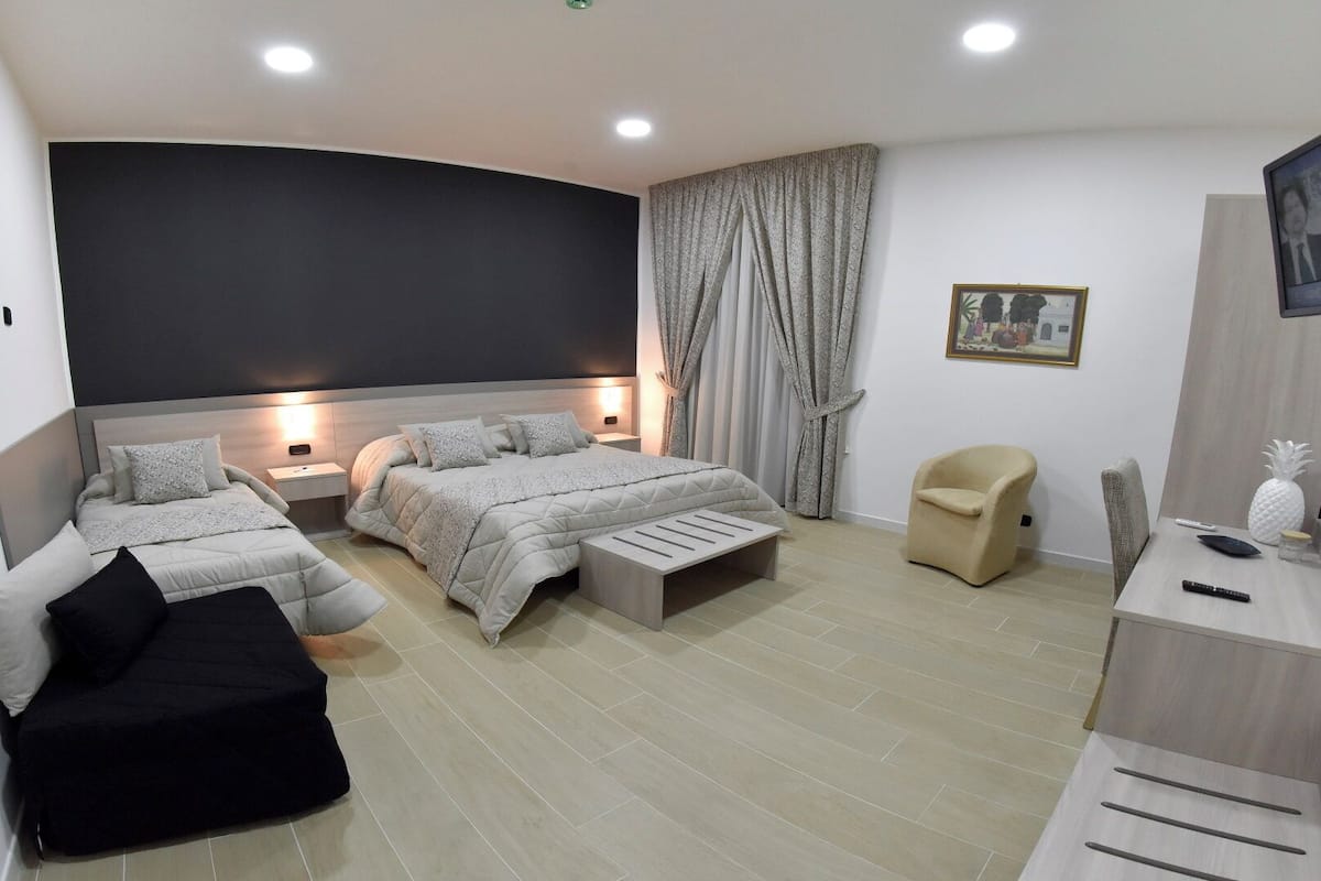 A modern bedroom with two beds, a sofa, a desk, and a TV.