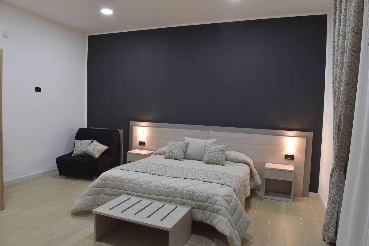 A modern bedroom with a large bed, bedside tables, a chair, and a nightstand.