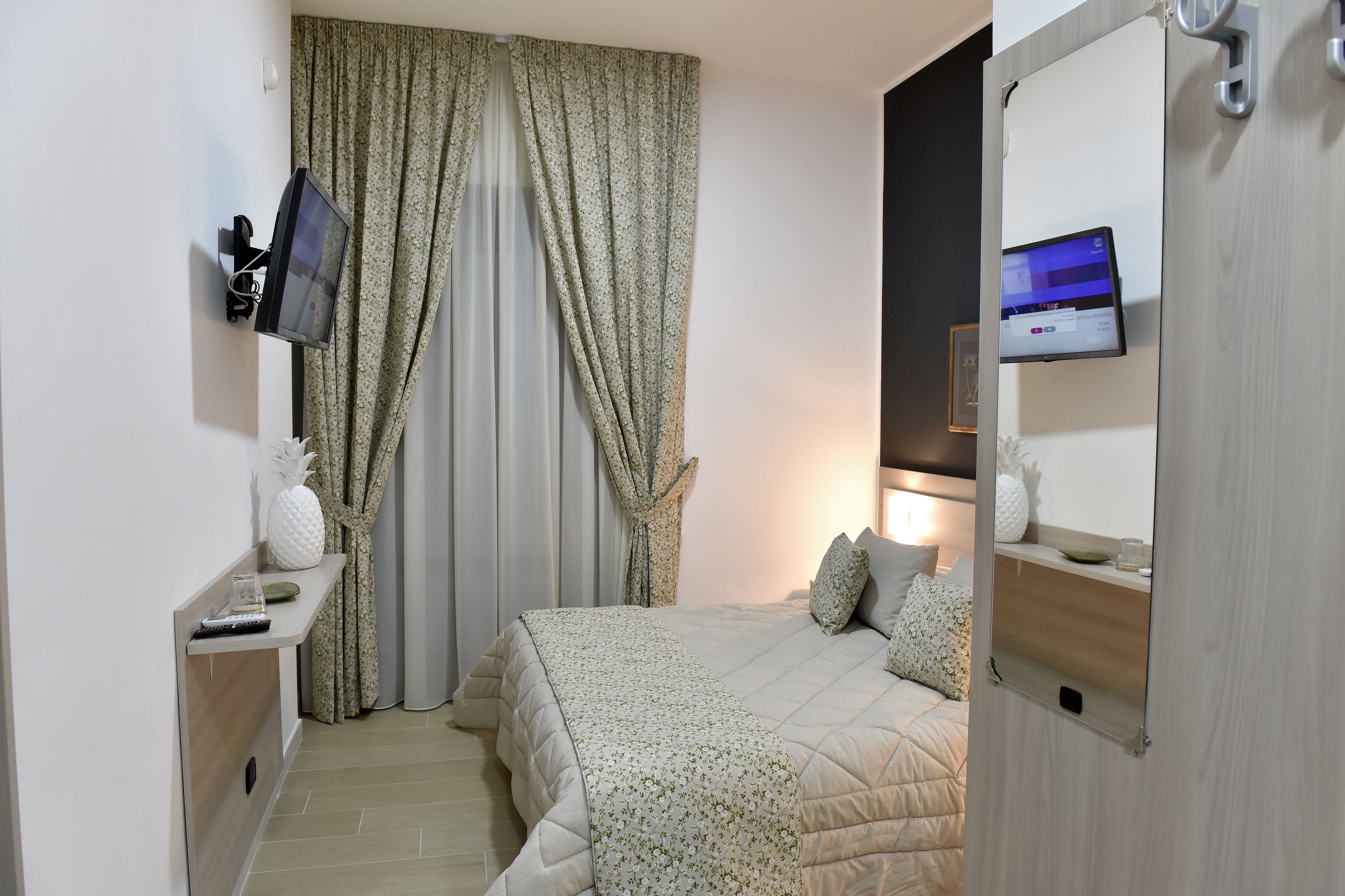 A hotel room with a bed, a TV mounted on the wall, a desk with a remote control, and a mirror.