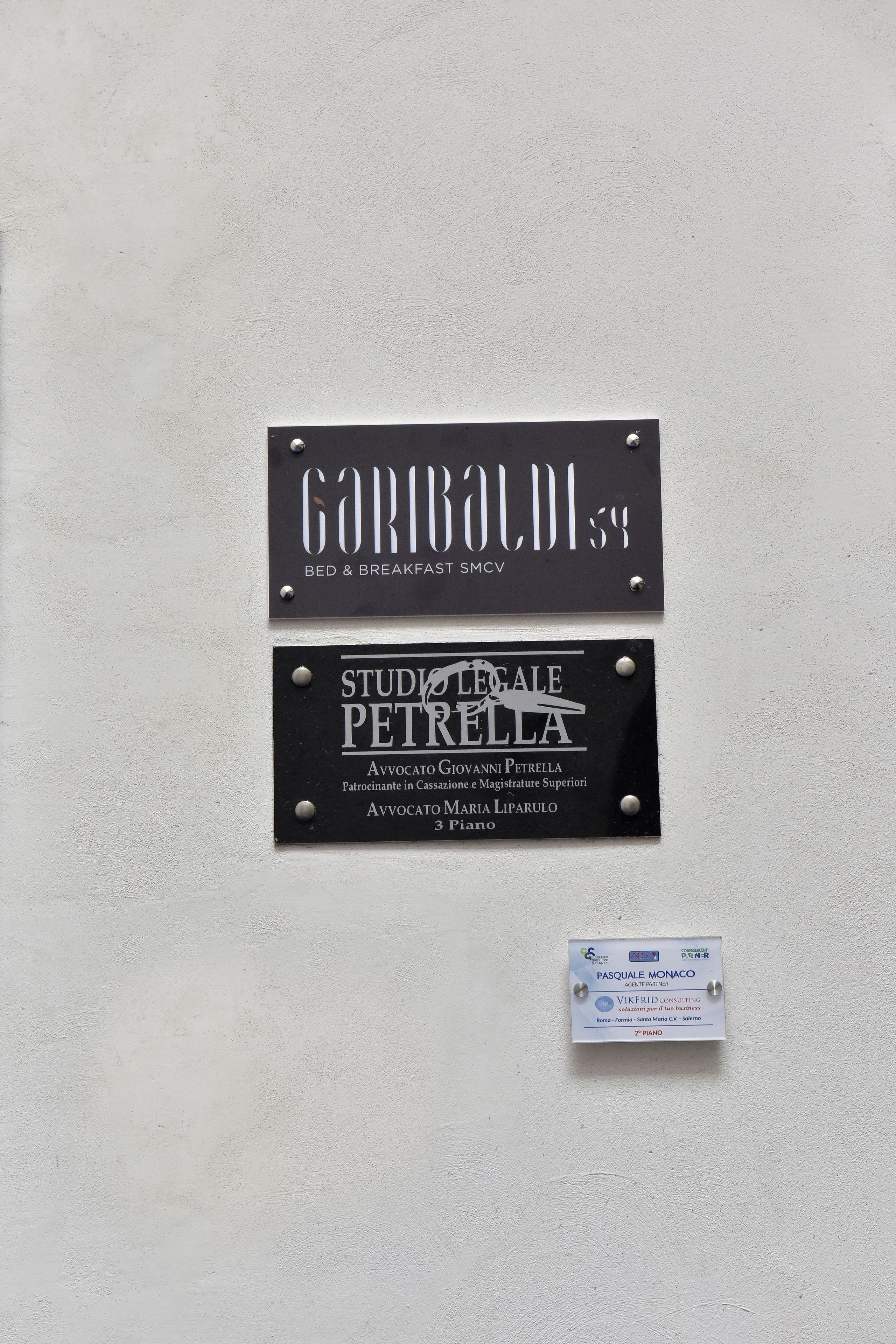 Tres letreros en una pared: GARIBALDI 54, STUDIO LEGALE PETRELLA y PASQUALE MONACO.