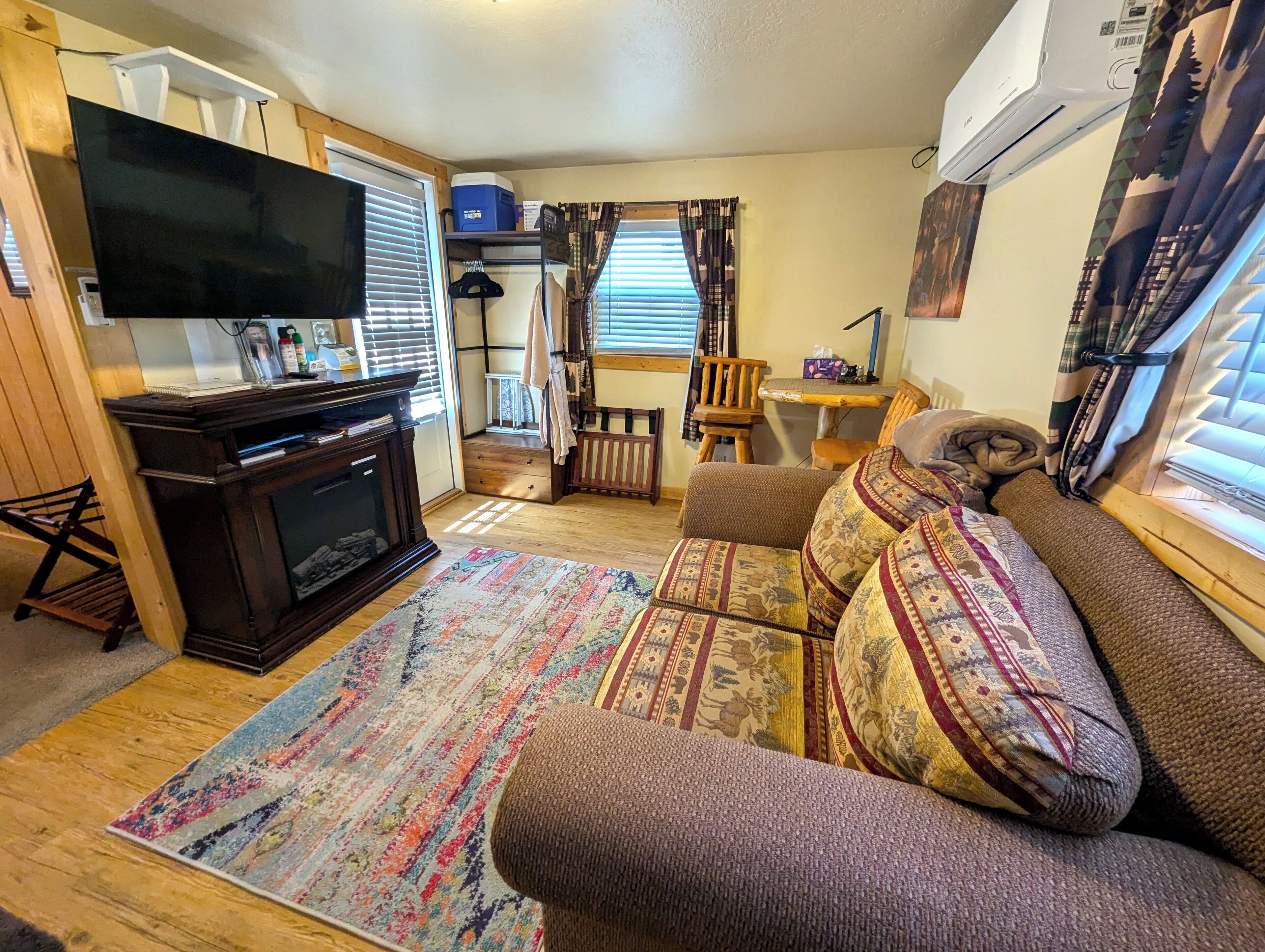 A cozy living room with a flat-screen TV, wooden furniture, a patterned rug, and a sofa with decorative pillows.