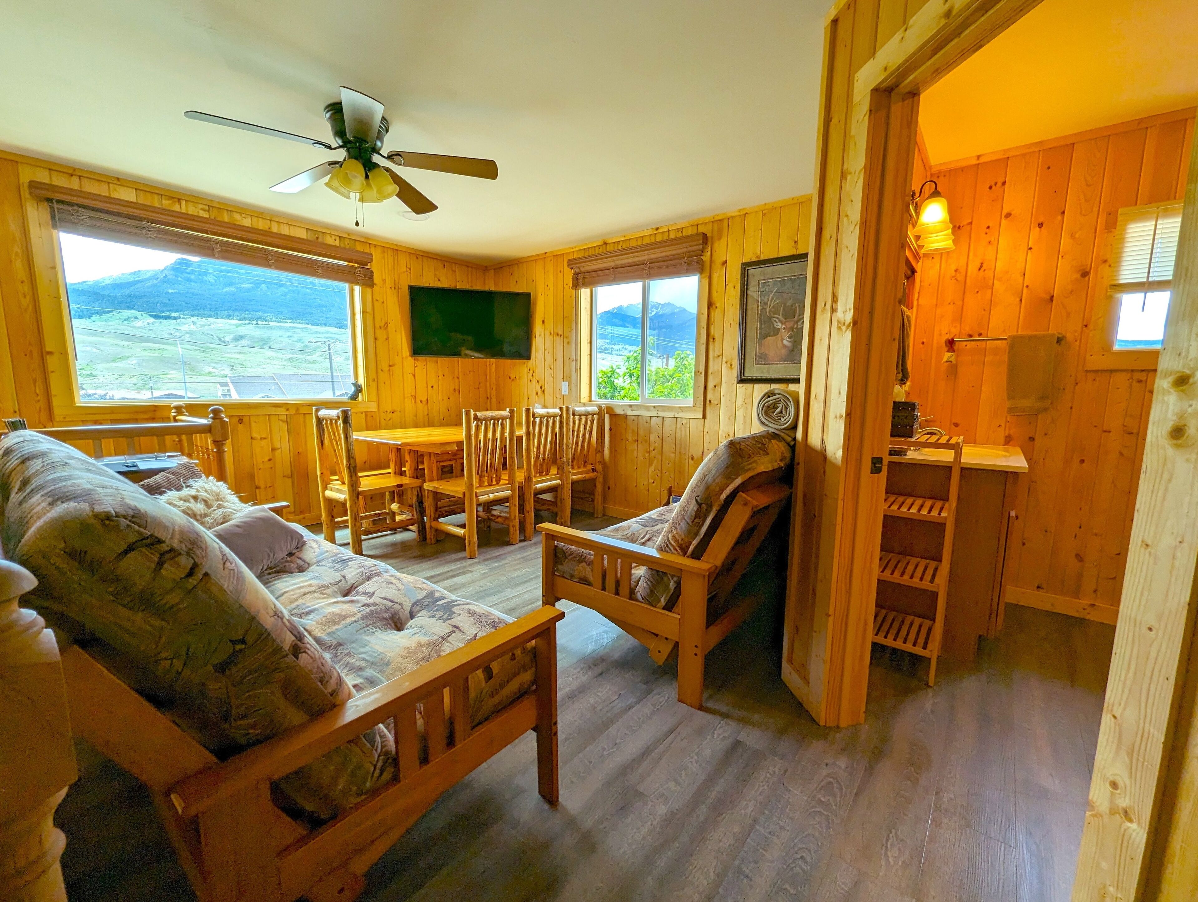 Interior acolhedor de uma cabana com uma mesa de jantar de madeira, cadeiras, um sofá e um ventilador de teto.