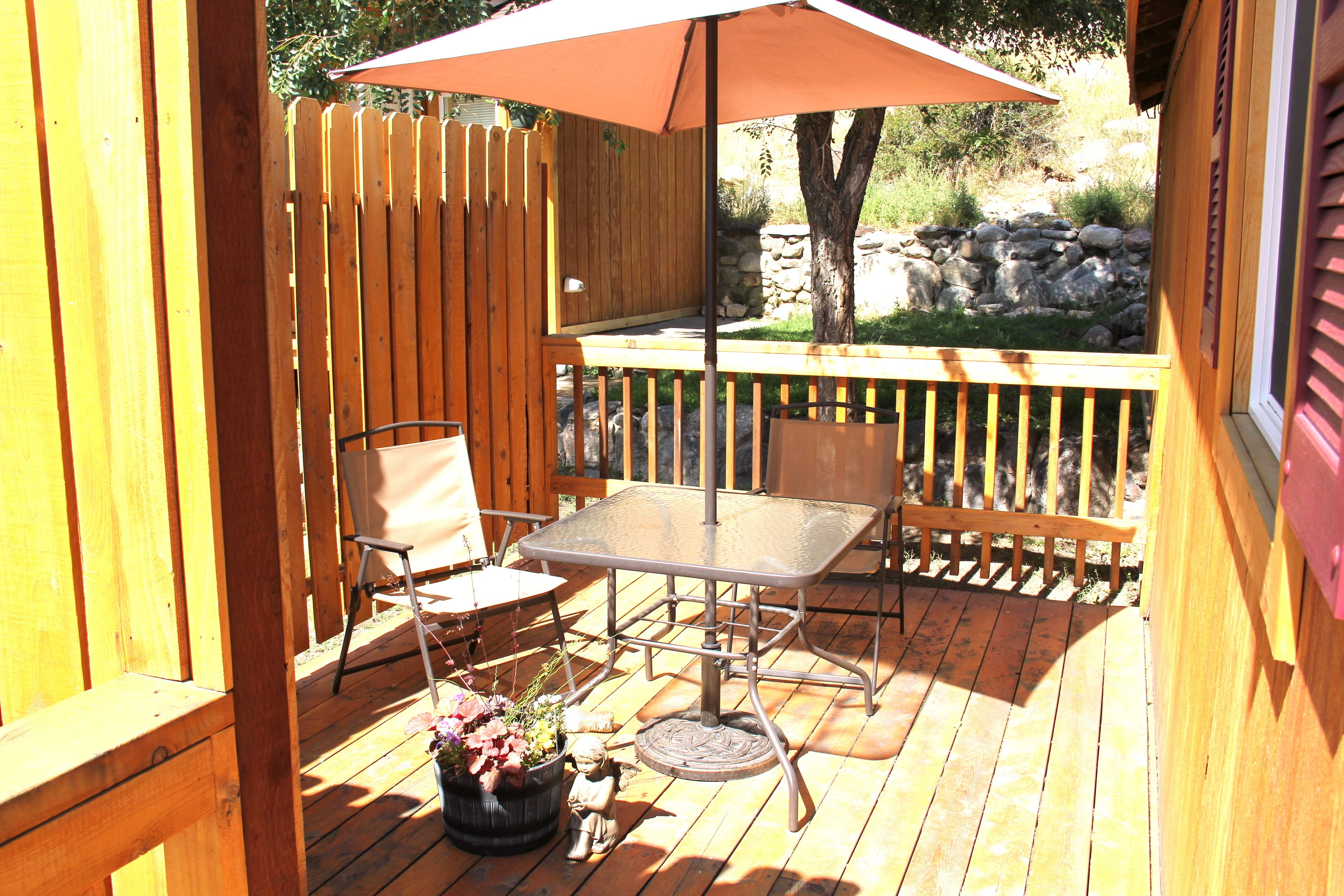 A wooden deck with a metal table and chairs, a potted plant, and a wooden fence.
