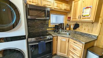 A compact kitchen with a built-in washer and dryer, stainless steel appliances, wooden cabinets, granite countertops, and a check-out checklist on the wall.