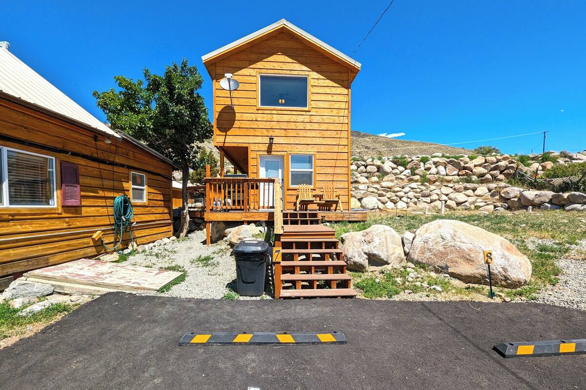 A wooden cabin with a deck, a satellite dish, and a trash bin.