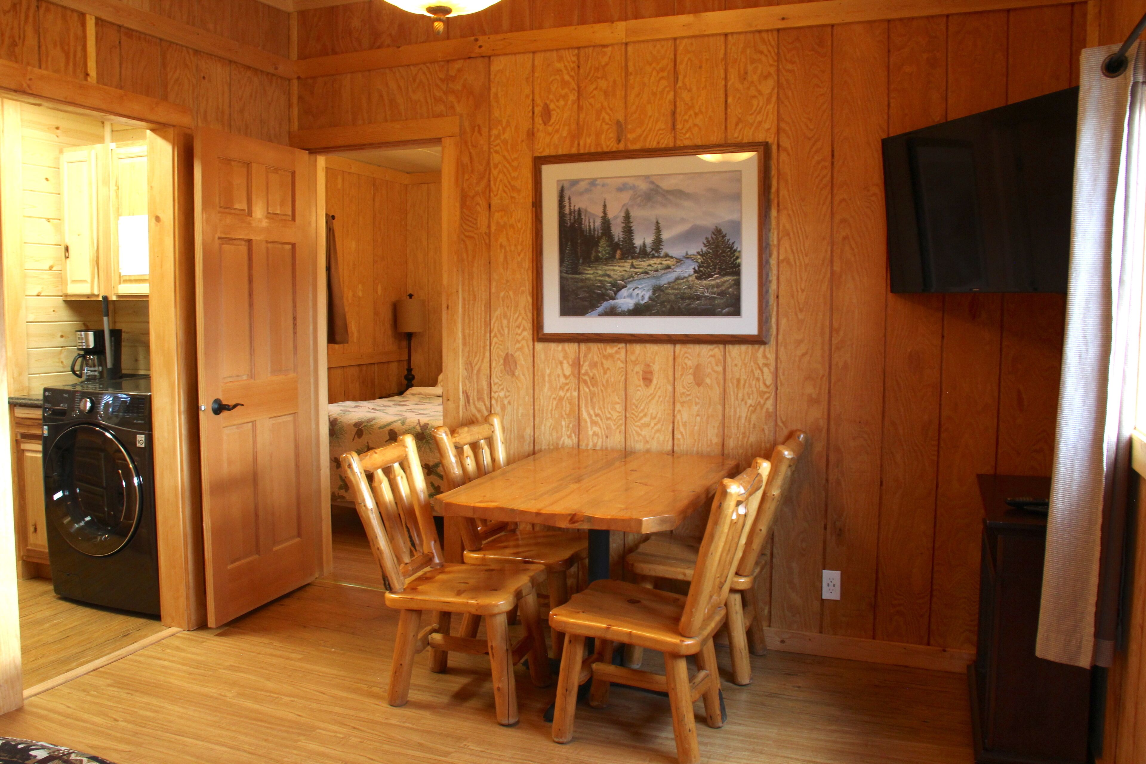 Un intérieur en bois avec une table et des chaises, un tableau accroché au mur et un lave-linge dans un coin.