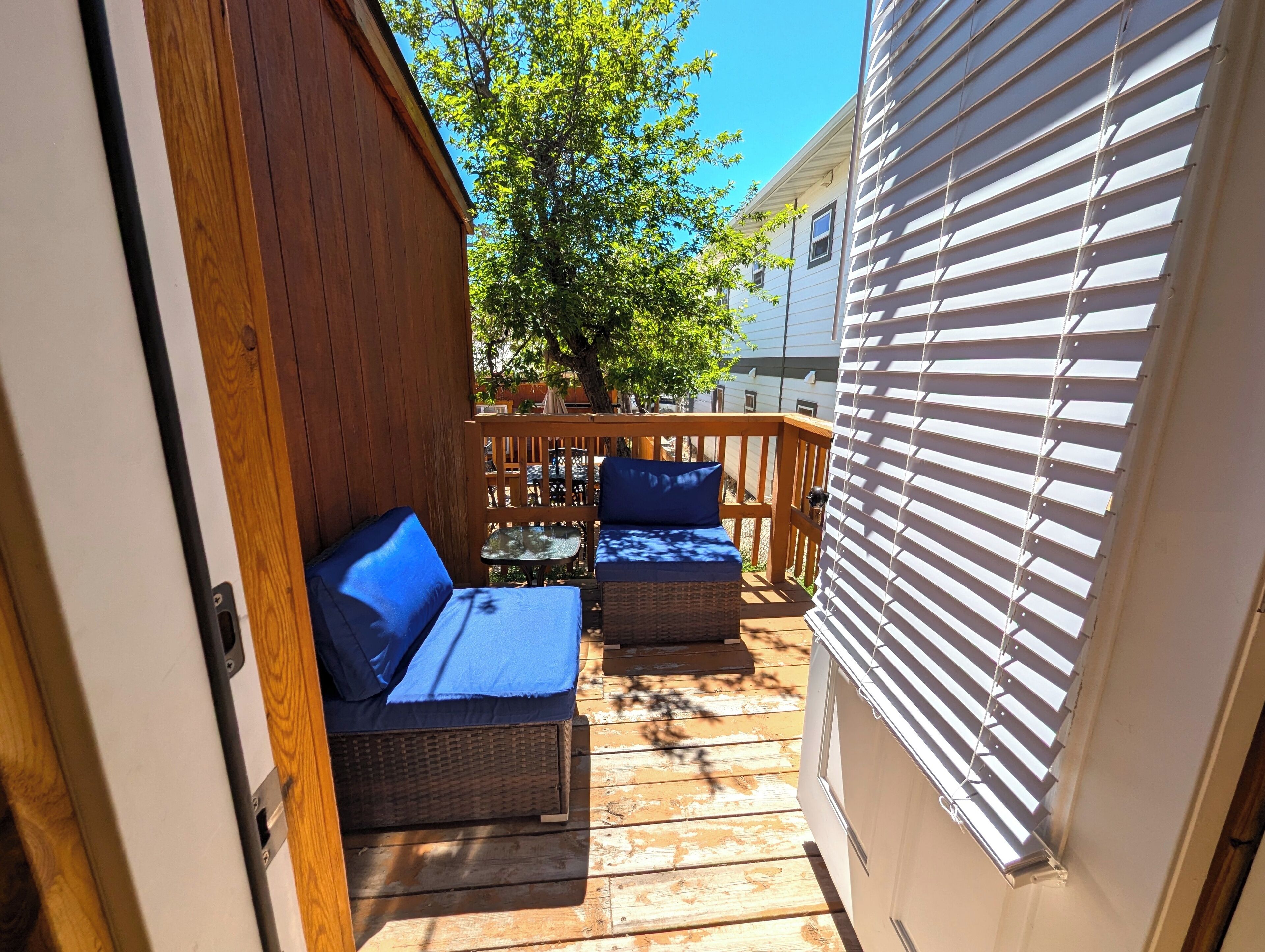 Une terrasse en bois avec deux canapés en osier et une petite table, une clôture en bois et un bâtiment blanc aux bardages horizontaux.