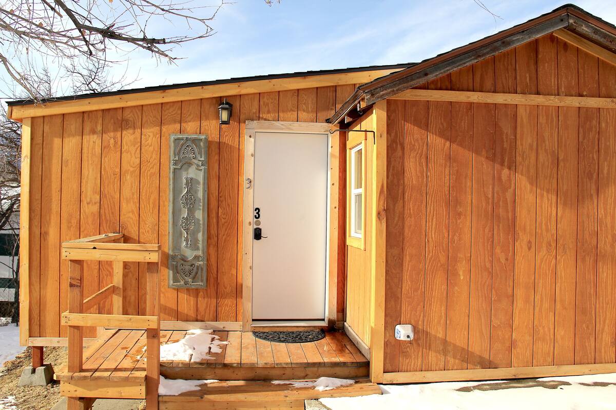 A wooden cabin with a door marked "3", a small porch, and a metal decorative panel.
