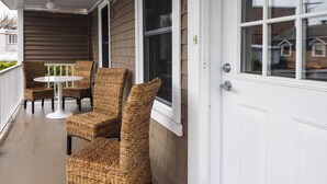 A covered porch with wicker chairs and a small table, a white door, and a window with blinds.