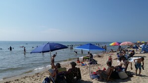 Ein belebter Strand mit badenden und sonnenbäudelnden Menschen unter Sonnenschirmen.