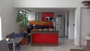 A compact kitchen with a red accent wall, a built-in microwave, and a refrigerator. A dining area with a blue table and chairs is adjacent to the kitchen. - Comfort Campestre (Tabio)